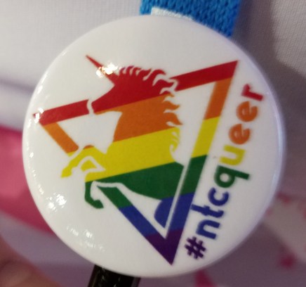 A pin with a rainbow unicorn and triangle, and #NTCQueer